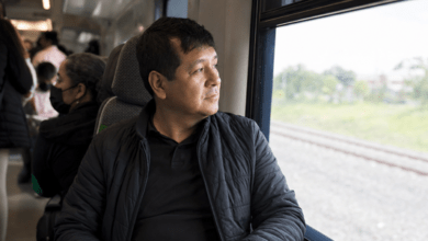 Pasajero mira por la ventana de un tren interurbano mientras sostiene su teléfono